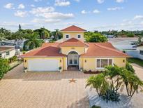 Stunning yellow house with red roof, brick driveway, and palm trees under sunny sky in Bellaire Beach at 108 24Th St, Belleair Beach, FL 33786
