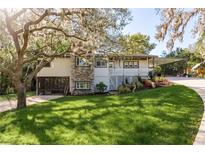 Charming two-story home featuring a stone facade, carport, landscaped front yard, and mature trees at 317 Old East Lake Rd, Tarpon Springs, FL 34688