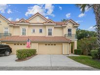 Charming townhome featuring a red tile roof, two-car garage, and beautifully landscaped front yard with an American flag at 2676 Tanglewood Trl, Palm Harbor, FL 34685