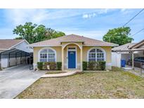 Charming single-story home featuring a blue door, arched windows, and manicured landscaping at 6920 N Hubert Ave, Tampa, FL 33614