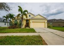 Charming yellow single-Gathering home featuring a two-car garage and lush landscaping at 12720 Whitney Meadow Way, Riverview, FL 33578