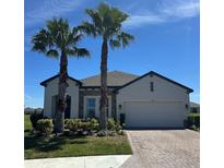 Beautiful single-story home boasts a brick driveway, two-car garage, manicured landscaping, and two mature palm trees at 1904 146Th E Ter, Parrish, FL 34219