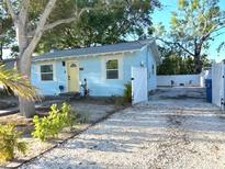 Charming, light-blue single-story home with a gravel driveway, lush trees, and a bright yellow door at 801 53Rd N Ter, St Petersburg, FL 33703