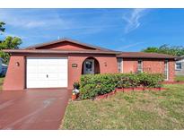 Charming one-story home with colorful red exterior, manicured lawn, and attached garage under a bright blue sky at 10035 Cherry Creek Ln, Port Richey, FL 34668