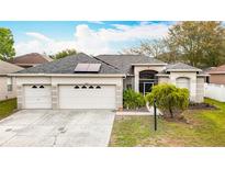 Inviting home exterior with a three-car garage, manicured lawn, and solar panels for sustainability at 4262 Larkenheath Dr, Spring Hill, FL 34609