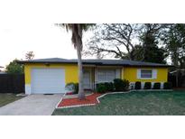 Charming single-story home featuring a bright yellow exterior, well-maintained landscaping, and an attached one-car garage at 2118 Ne Coachman Rd, Clearwater, FL 33765