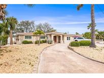 Charming single-story home featuring a well-manicured yard with lush tropical landscaping and a long concrete driveway at 2490 E Vina Del Mar Blvd, St Pete Beach, FL 33706