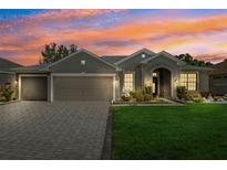 Charming single-story home featuring a three-car garage, lush lawn, and a brick driveway with a beautiful sunset backdrop at 12308 Bramfield Dr, Riverview, FL 33579