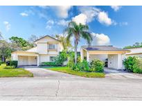 Inviting two-story home featuring a well-manicured lawn, lush landscaping, and dual carports for ample parking at 2581 Forest Run Ct, Clearwater, FL 33761