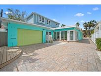 Bright turquoise home with a large brick driveway, a green garage door, and ample parking space at 106 23Rd Ave, St Pete Beach, FL 33706