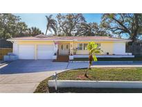 Charming yellow single-story home featuring a red tile roof and double-door entryway, showcasing its curb appeal at 1201 Kapok Kove Cir, Clearwater, FL 33759