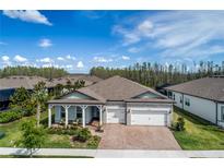 Inviting single-story home featuring a brick driveway, two-car garage, and charming covered porch with stone accents at 18636 Sailors Delight Pass, Land O Lakes, FL 34638