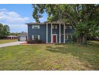 Inviting two-story home featuring a charming red door, stately columns, and a beautiful mature shade tree at 4125 89Th E St, Palmetto, FL 34221