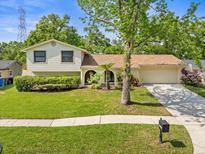 Charming two-story home with mature trees, lush green lawn, and a welcoming front entrance at 16320 Bonneville Dr, Tampa, FL 33624