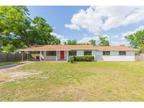 Charming single-story home featuring a bright red door, carport, and a spacious front yard with mature trees at 3502 Bloomingdale Ave, Valrico, FL 33596