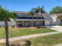 Two-story home with manicured lawn and landscaping, bench on front porch, and an attached garage; palm trees provide shade at 8326 Archwood Cir, Tampa, FL 33615