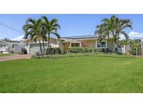 Inviting single-story home with a lush green lawn, tropical palm trees, and a two-car garage at 1361 46Th Ne Ave, St Petersburg, FL 33703
