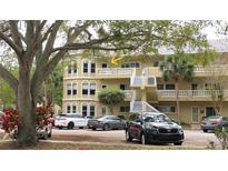 Three story condo building with yellow paint and white trim, accented by lush green trees and parked cars at 2221 Norwegian Dr # 43, Clearwater, FL 33763