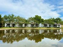 Waterfront two-story condo building reflected in a pond with mature trees and blue skies at 3821 N Oak Dr # J31, Tampa, FL 33611