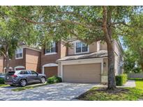 Two story tan home featuring an attached two car garage and mature shade tree at 4920 Pond Ridge Dr, Riverview, FL 33578