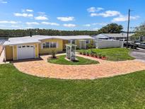 Charming yellow waterfront home featuring a brick circular driveway and well-manicured lawn at 109 Carmelina St, Ruskin, FL 33570