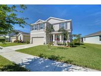 Charming two-story home with a well-manicured lawn, gray facade, and a two-car garage under a clear blue sky at 5325 Thistle Field Ct, Wesley Chapel, FL 33545