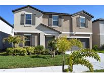 Charming two-story home boasts a well-manicured lawn, complemented by lush tropical landscaping, and a gray front door at 12957 Wildflower Meadow Dr, Riverview, FL 33579
