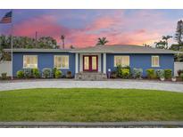 Charming blue home featuring a well-manicured lawn and inviting red double-door entry with a beautiful sunset sky at 301 71St S St, St Petersburg, FL 33707