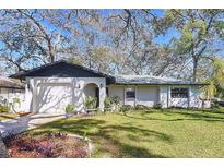 Charming single-story home with a well-manicured lawn and an attached garage, all shaded by mature trees at 2004 Nobleton Ave, Spring Hill, FL 34608