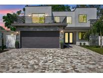 Modern two-story home featuring a balcony, stone accents, a gray garage door, and a patterned brick driveway at 2140 Catalina Dr, Clearwater, FL 33764