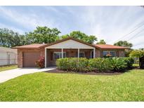 Charming brick home featuring a well-manicured lawn, flowering bushes and an attached one-car garage at 4812 Wynwood Dr, Tampa, FL 33615