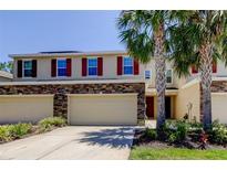 Inviting townhome with tan exterior, stone accents, two-car garage, and beautiful landscaping with palm trees at 13217 Canopy Creek Dr, Tampa, FL 33625
