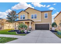 Two-story home with tan exterior, dark garage, landscaped front yard, and beautiful lawn at 21832 Crest Meadow Dr, Land O Lakes, FL 34637