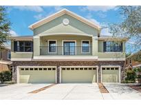 Two story home featuring a balcony, light green stucco, stone accents, and a three car garage at 5714 Kingletsound Pl, Lithia, FL 33547