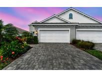 Two-car garage with a brick driveway and lush landscaping under a beautiful sunset sky at 12408 Palatka Dr, Venice, FL 34293