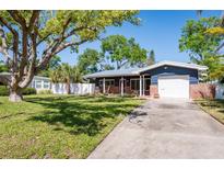 Charming home featuring a lush green lawn, mature shade trees, and a quaint front porch with a rocking chair at 2019 Inner S Cir, St Petersburg, FL 33712