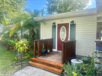 Charming home entrance featuring a wooden porch, red door, green shutters, and lush tropical landscaping at 7110 N Rome Ave, Tampa, FL 33604