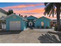 Charming turquoise home with well-manicured front yard, palm tree, and a two car garage on a beautiful day at 321 Bahia Vista Dr, Indian Rocks Beach, FL 33785