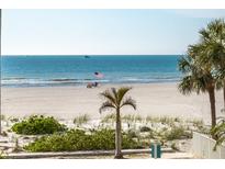 Wide beach view with an American flag, blue water, palm trees, and beautiful beach vegetation at 1390 Gulf Blvd # 104, Clearwater, FL 33767