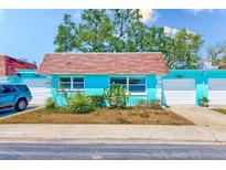 Charming light-blue home featuring a red-tiled roof and attached garage, set against a backdrop of lush green trees at 7081 Lafayette N, Pinellas Park, FL 33781