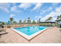 Community swimming pool surrounded by lounge chairs, palm trees, and clear skies on a sunny day at 7100 Sunset Way # 303, St Pete Beach, FL 33706