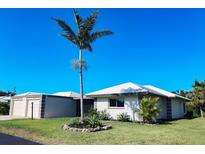 Charming single-story home featuring a well-manicured lawn and a large palm tree against a clear blue sky at 208 Villa Dr # 208, Osprey, FL 34229