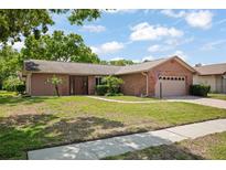 Charming single-story home featuring a brick facade, manicured lawn, and mature trees under a blue sky at 2859 Thistle N Ct, Palm Harbor, FL 34684