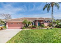 Charming single-story home featuring a beautiful lawn, colorful landscaping, and a welcoming pink garage door at 3136 Sandhill Dr, Holiday, FL 34691