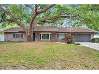 Charming brick home featuring a lovely, large tree, well-maintained lawn and an attached two-car garage at 1308 W Perdiz St, Tampa, FL 33612