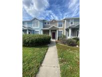 A colorful two-story townhome with a landscaped front yard and a concrete walkway under a blue cloudy sky at 3441 Santa Rita Lane, Land O Lakes, FL 34639