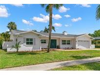 Charming white brick home with a well-manicured lawn, palm trees and a light gray roof at 3945 Versailles Dr, Tampa, FL 33634