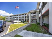 Three-story building featuring an American flag, garden beds, and a parking lot under a clear blue sky at 2229 Americus W Blvd # 25, Clearwater, FL 33763