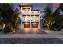 Stunning three-story home with private balconies, two-car garage, and brick driveway at sunset at 311 Spring Ave, Anna Maria, FL 34216