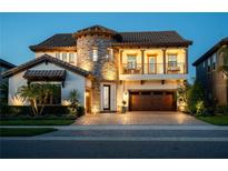 Elegant two-story home with a stone tower, balcony, tile roof, lush landscaping, and paver driveway at 21867 Amelia Rose Way, Land O Lakes, FL 34637